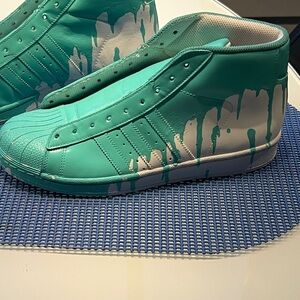Adidas Superstar high-tops featuring a teal drip pattern.